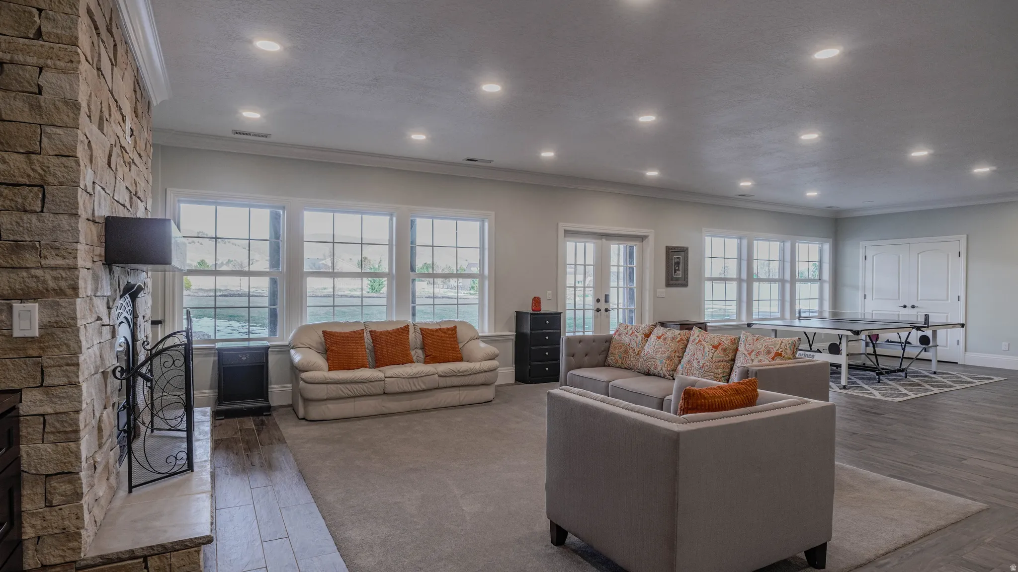 Living area featuring a stone fireplace, wood finished floors, crown molding, and recessed lighting