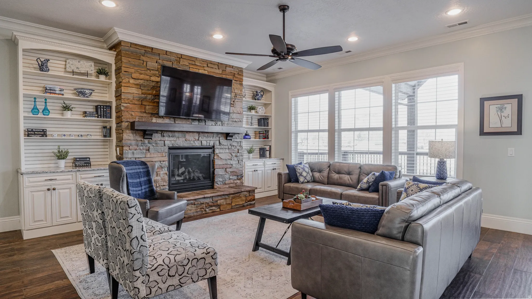 Living room with dark wood-style floors, crown molding, a stone fireplace, a ceiling fan, and recessed lighting