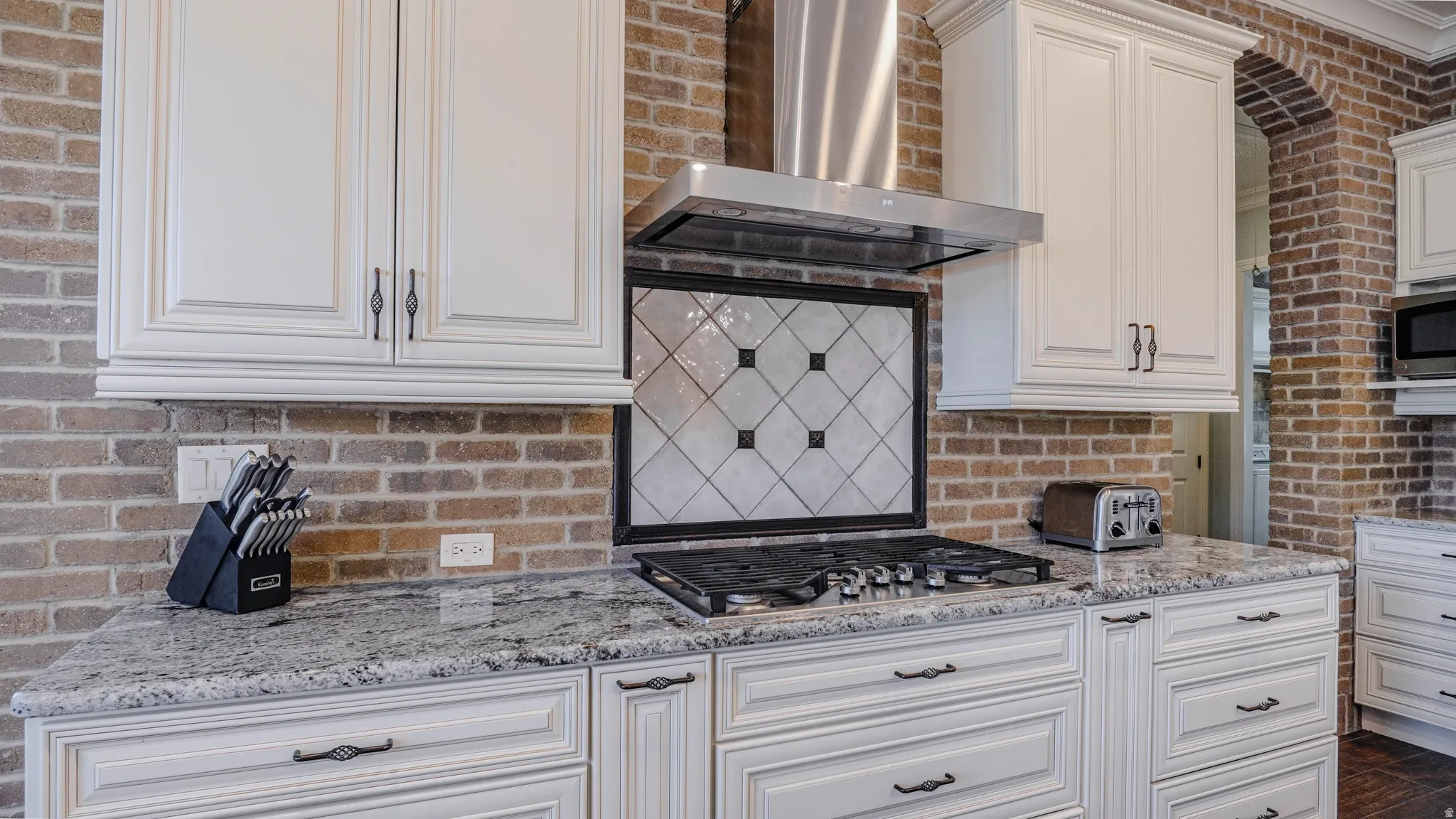 Kitchen with light stone counters, wall chimney exhaust hood, stainless steel appliances, white cabinetry, and tasteful backsplash