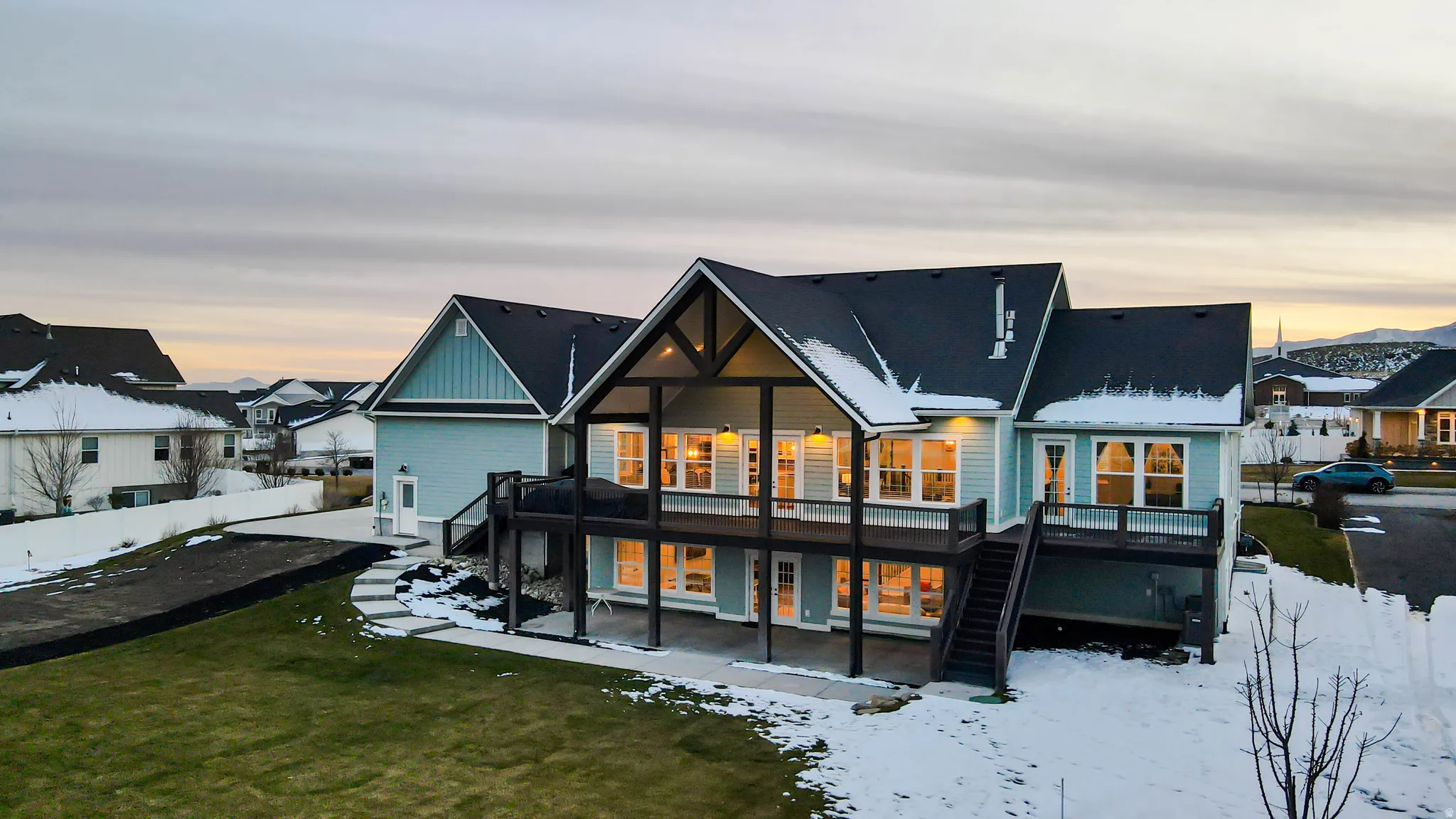 Snow covered back of property featuring stairway, a patio, a wooden deck, and a residential view
