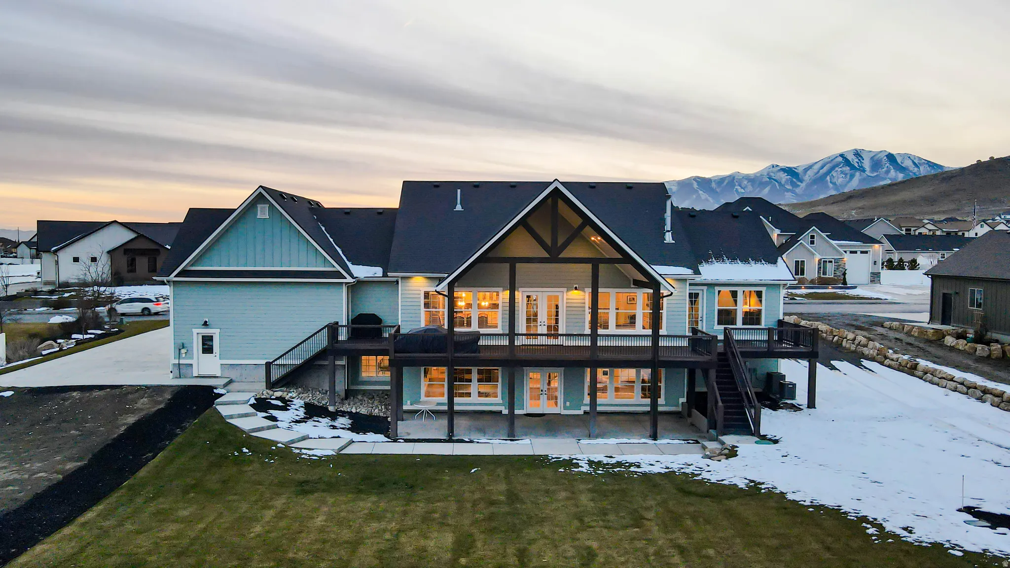 Snow covered house featuring stairway, a patio, a residential view, a deck, and board and batten siding