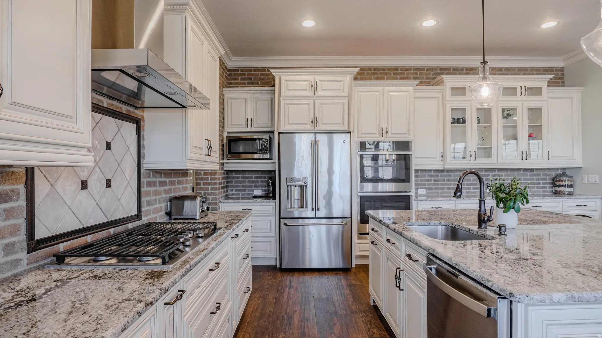 Kitchen with stainless steel appliances, light stone countertops, glass insert cabinets, wall chimney exhaust hood, and white cabinets