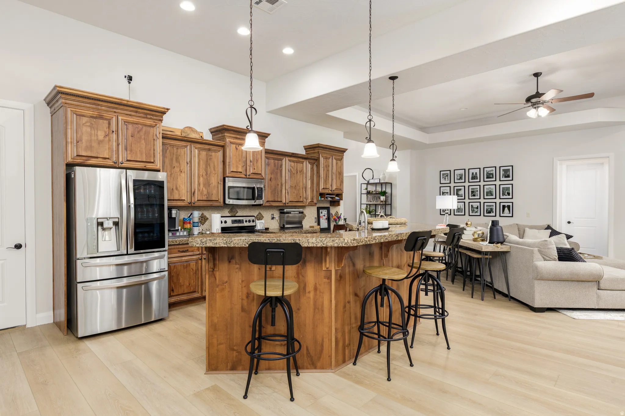 Kitchen with wood finish cabinets, stainless steel appliances, open floor plan, a center island with sink, and a raised ceiling