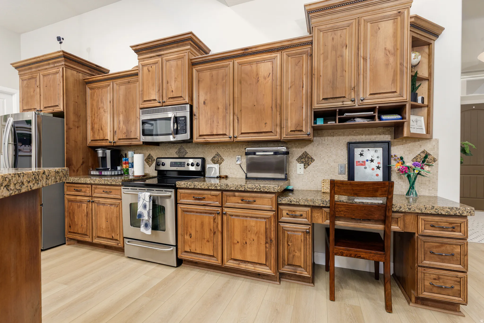 Kitchen with stainless steel appliances, wood finish cabinets, and light stone counters