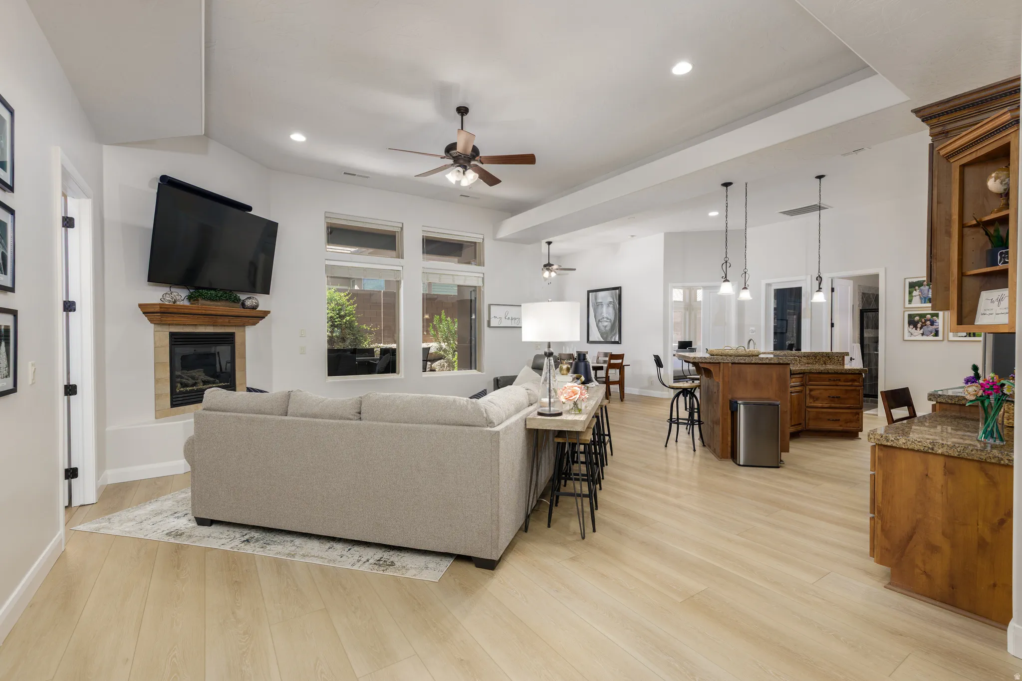 Living area with a glass covered fireplace, a ceiling fan, light wood-style flooring, and recessed lighting