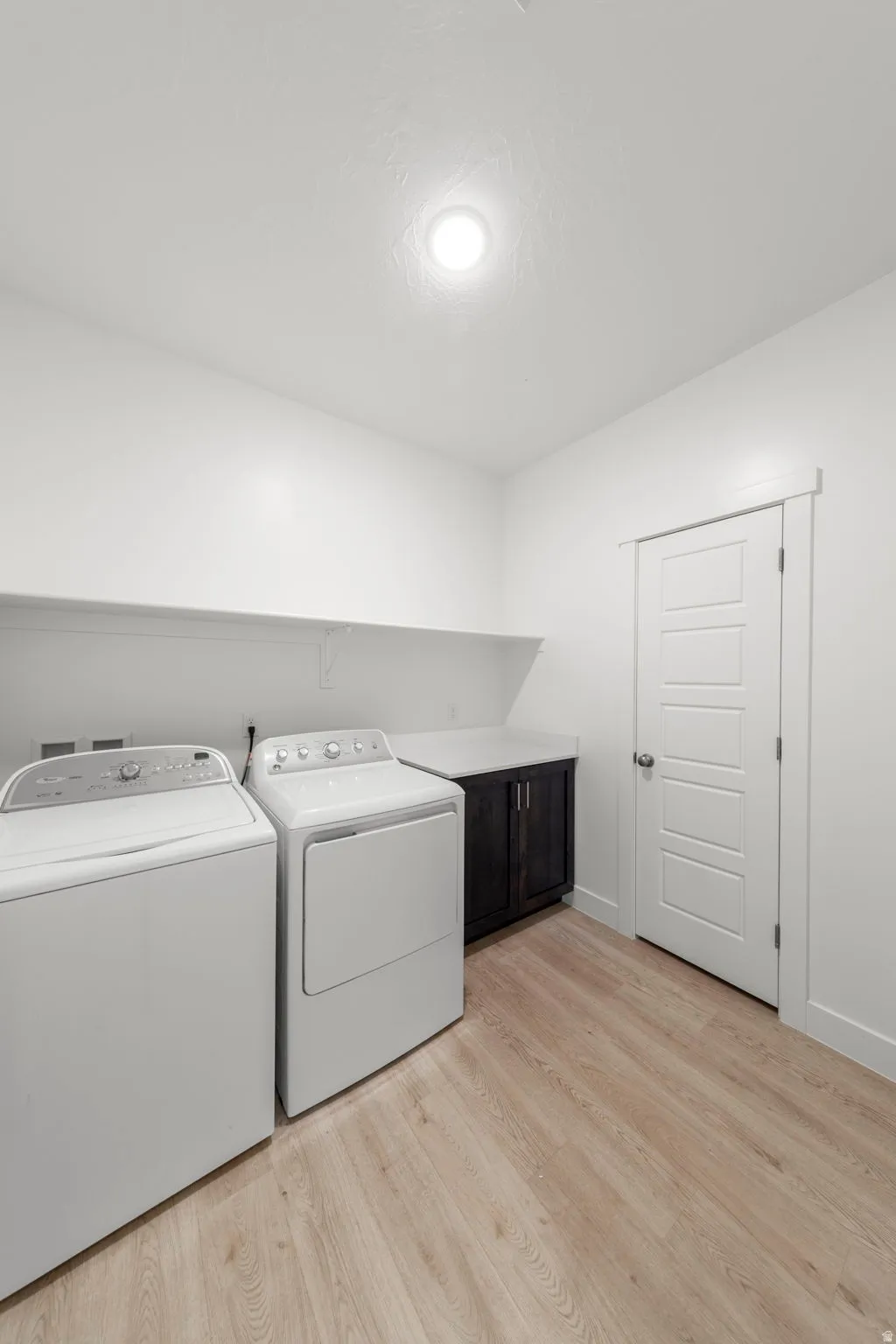 Laundry area featuring light wood-type flooring, washer and clothes dryer, and cabinet space