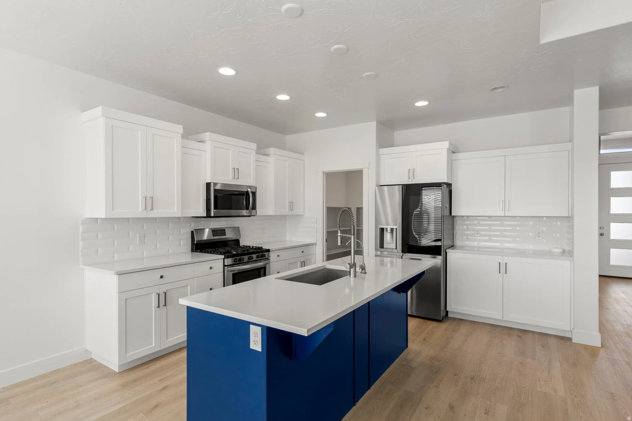 Kitchen with white cabinetry, appliances with stainless steel finishes, an island with sink, light wood-style flooring, and recessed lighting