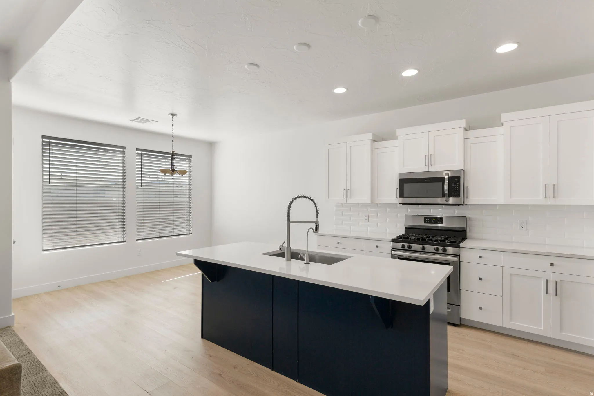Kitchen with stainless steel appliances, a center island with sink, light wood-type flooring, white cabinets, and recessed lighting