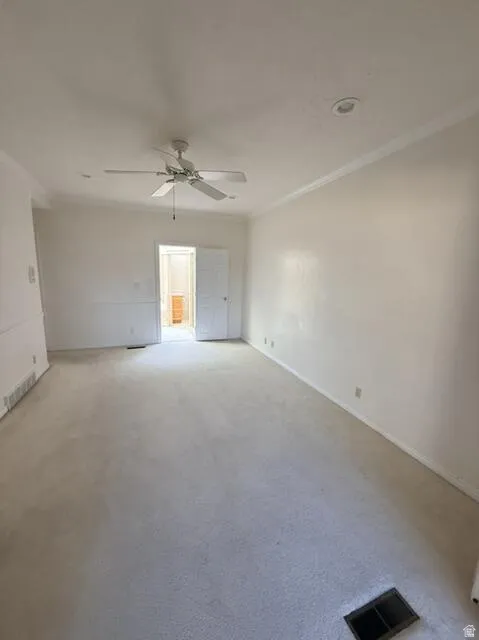 Empty room featuring crown molding, carpet flooring, and a ceiling fan