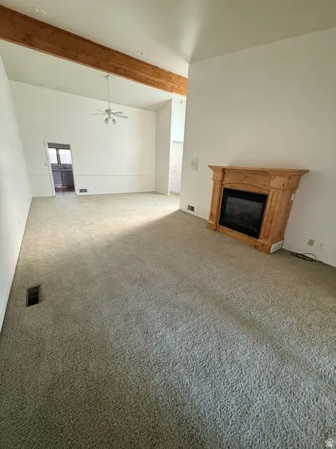 Unfurnished living room with a glass covered fireplace, carpet, beamed ceiling, and a ceiling fan