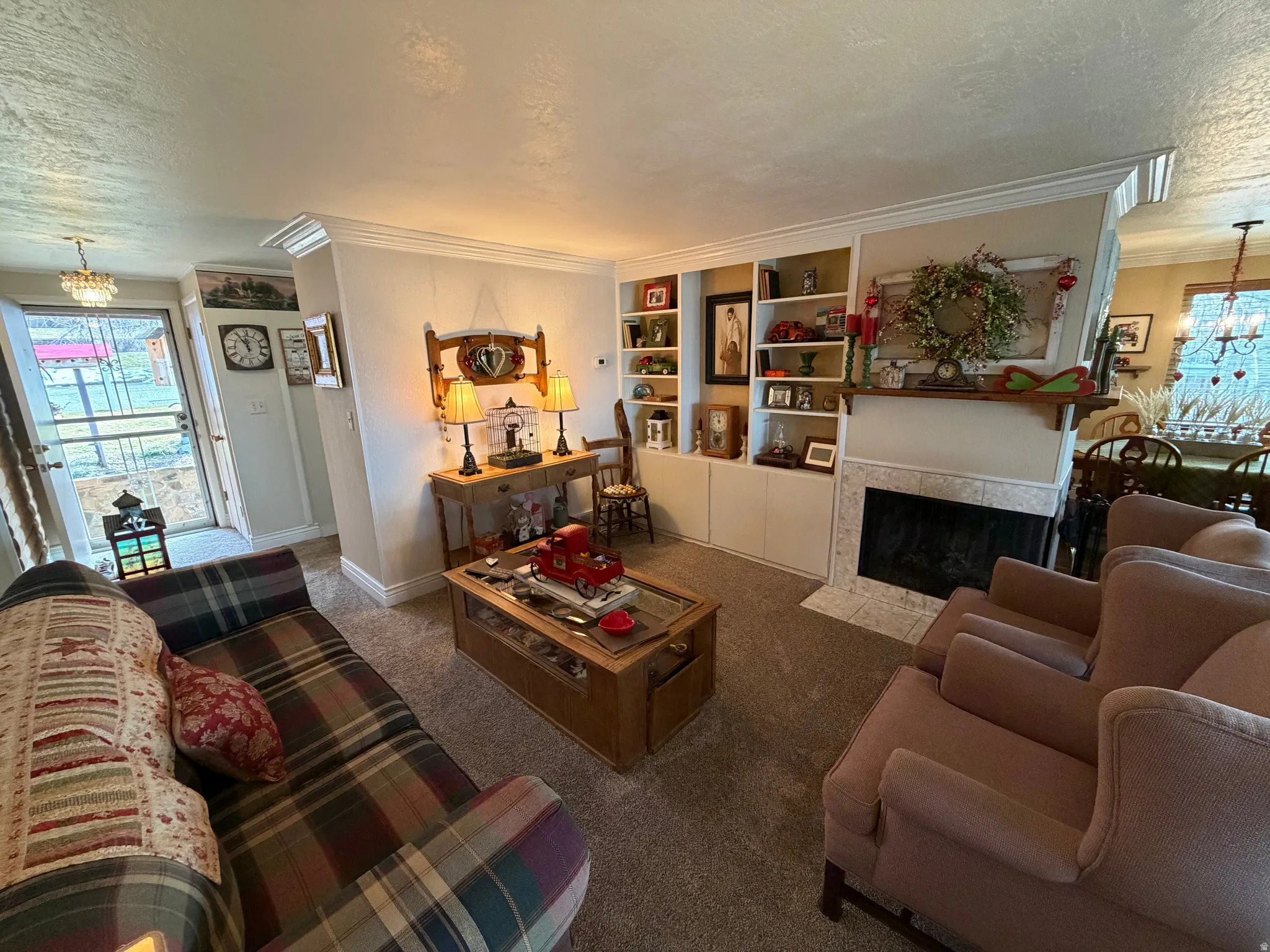 Carpeted living room with a chandelier, a textured ceiling, crown molding, built in shelves, and a tile fireplace