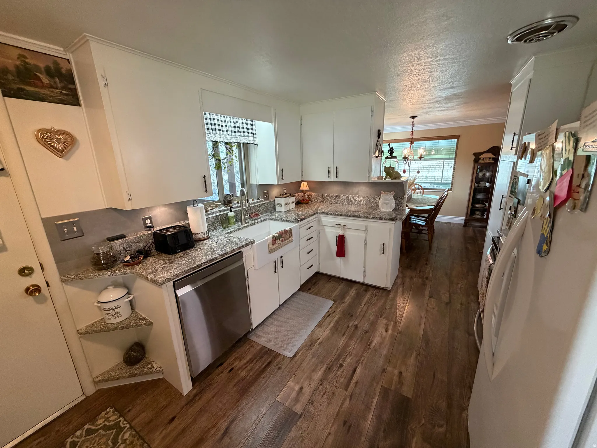Kitchen with white cabinets, freestanding refrigerator, a peninsula, stainless steel dishwasher, and light stone counters