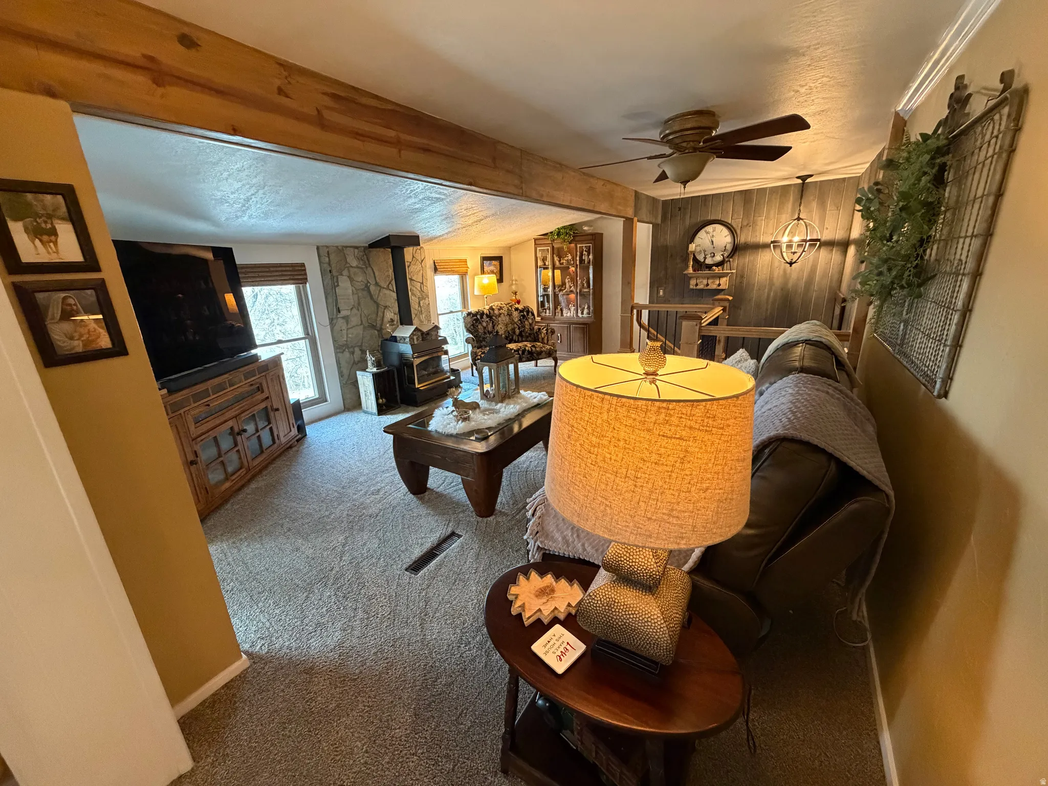 Living area featuring a wood stove, carpet floors, ceiling fan, and a textured ceiling