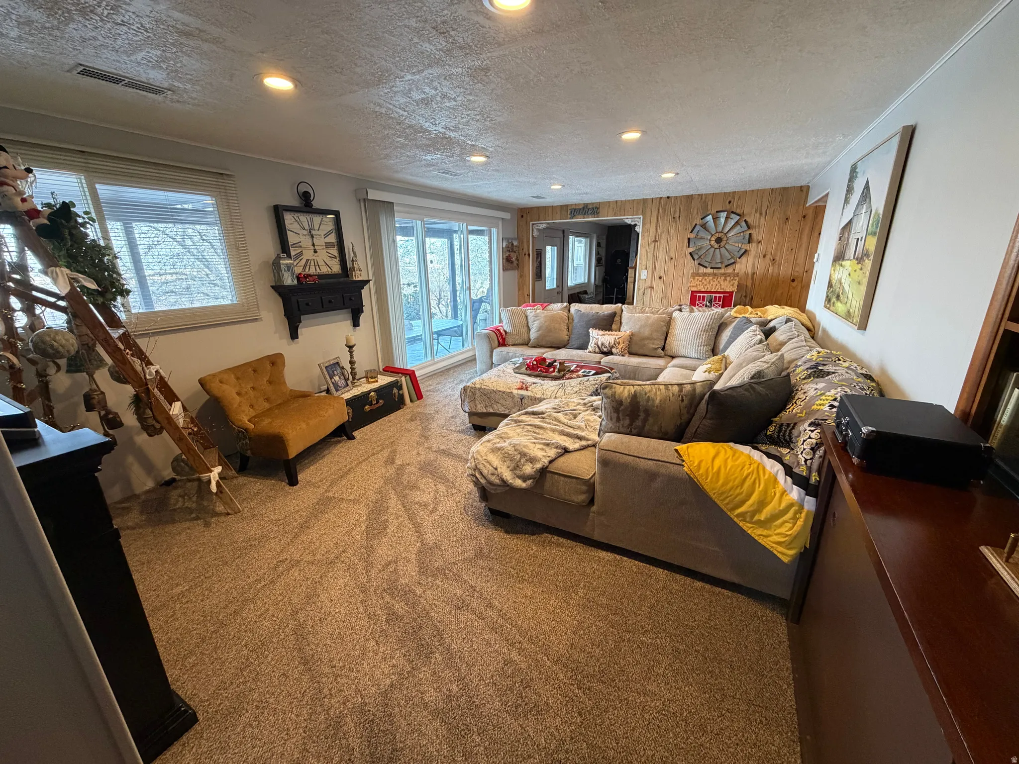 Living area featuring a textured ceiling, wooden walls, carpet floors, and recessed lighting