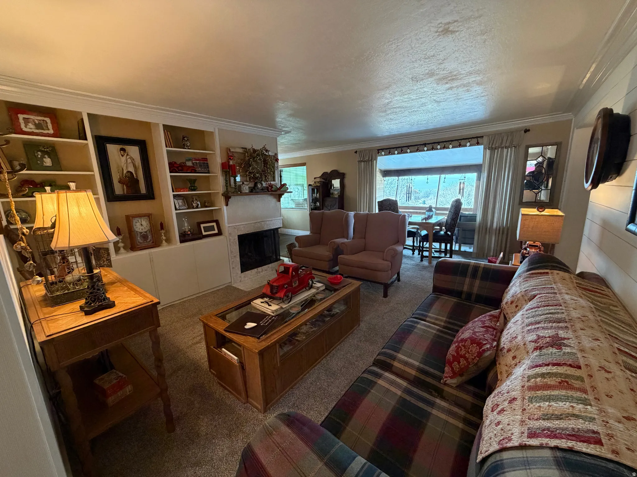 Carpeted living room featuring a fireplace with flush hearth, crown molding, built in features, and a textured ceiling