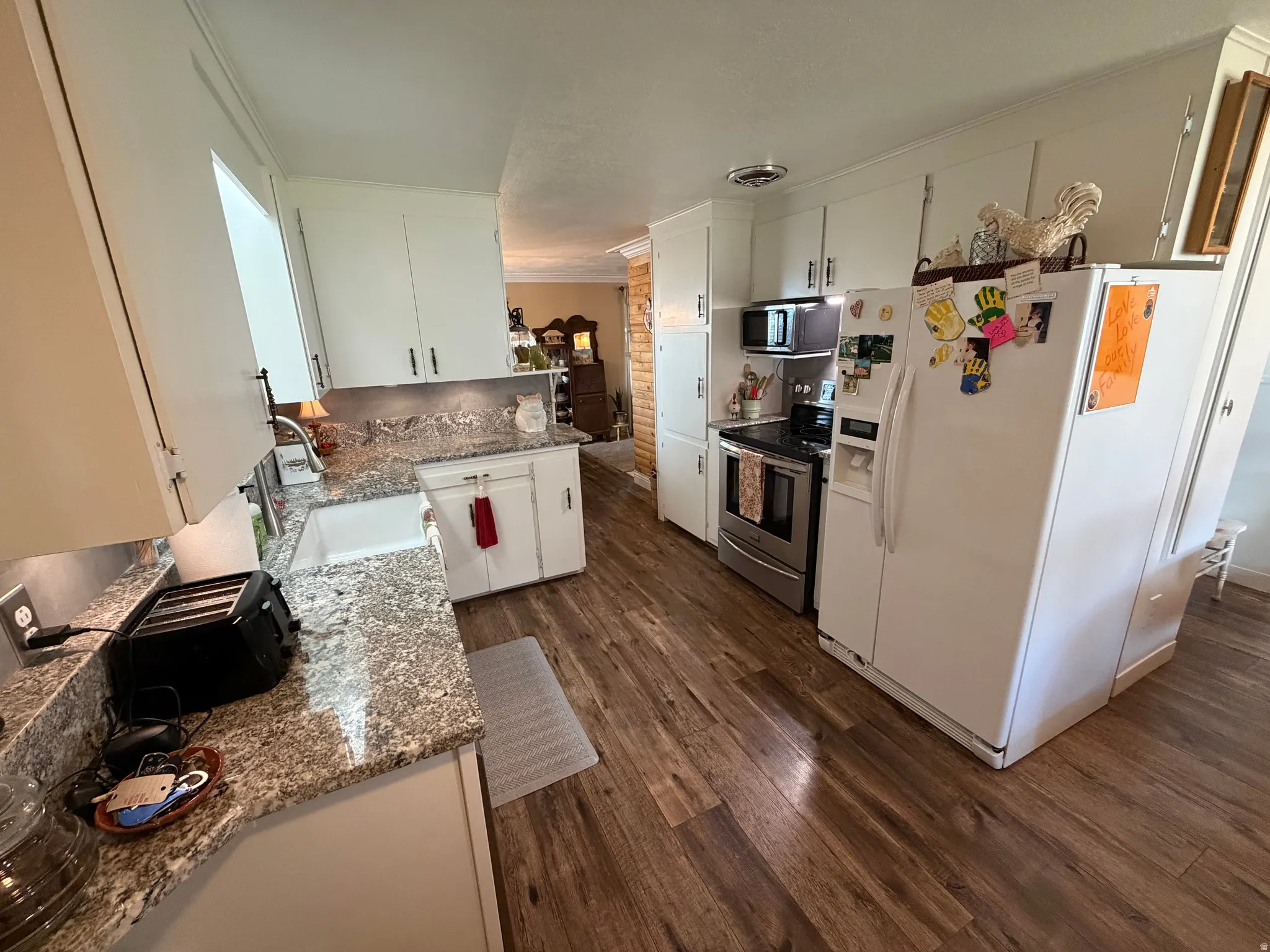 Kitchen featuring appliances with stainless steel finishes, white cabinets, light stone counters, dark wood-style flooring, and ornamental molding