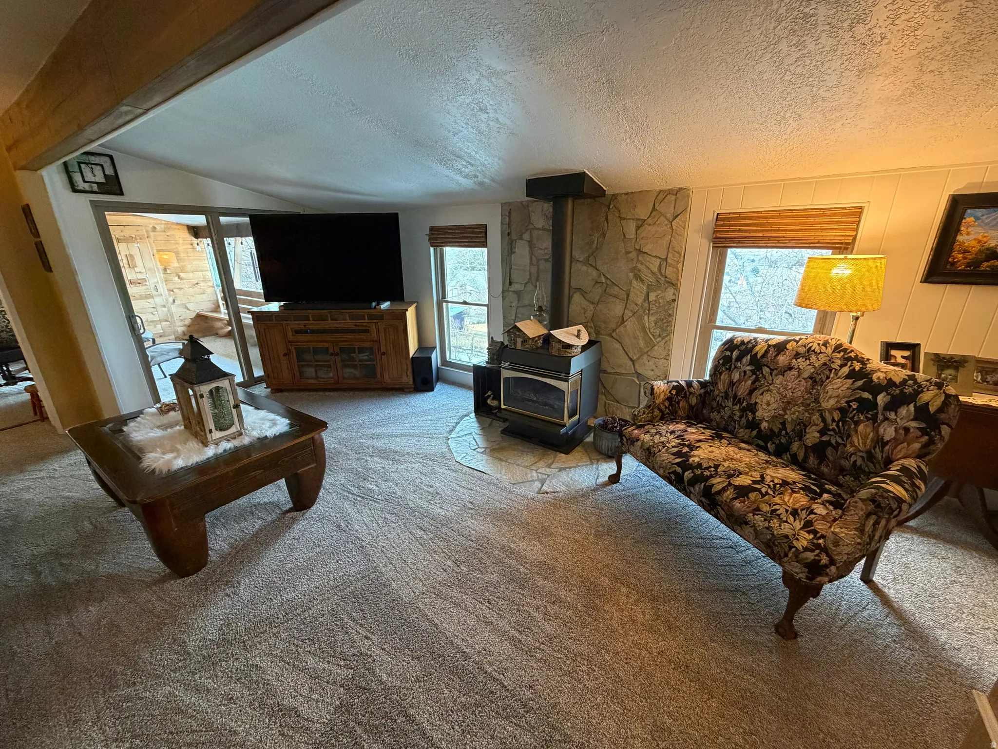 Living area with a wood stove, a textured ceiling, plenty of natural light, and carpet