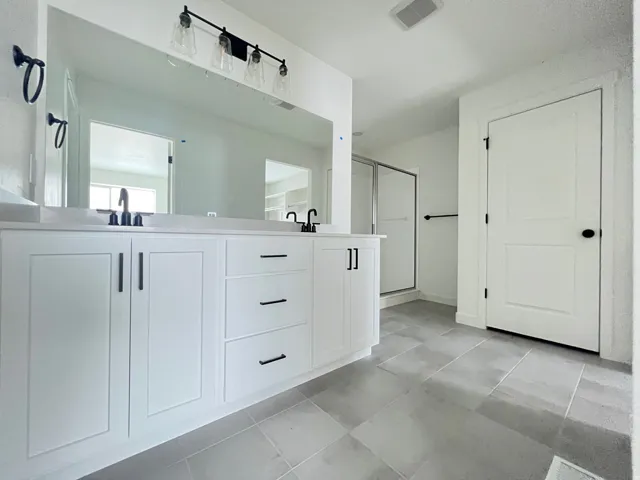 Bathroom with a shower stall, double vanity, and light tile patterned floors