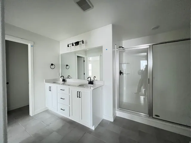 Bathroom featuring a shower stall, double vanity, and light tile patterned floors