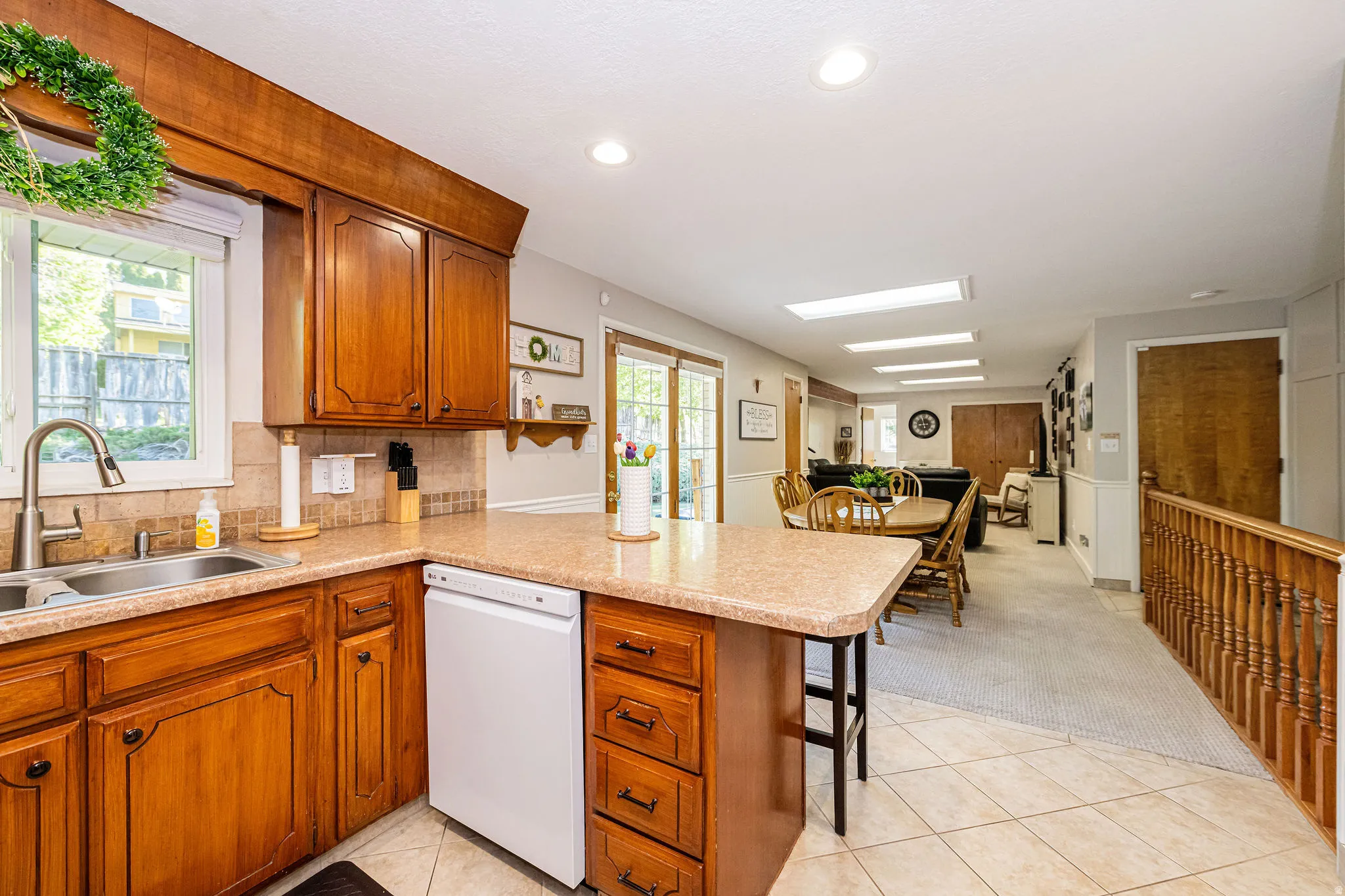 Kitchen with light colored carpet, dishwasher, brown cabinets, a peninsula, and light countertops