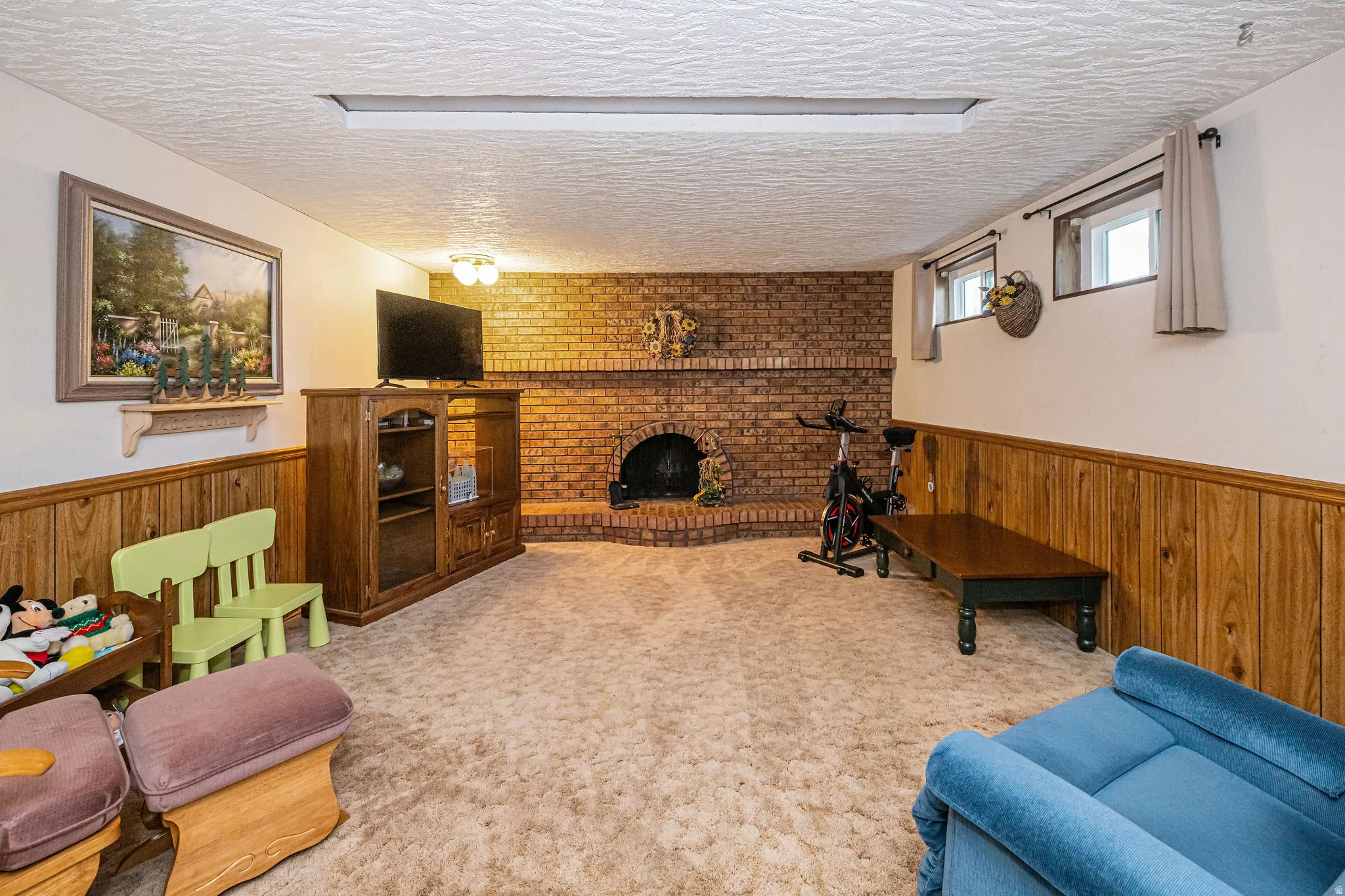 Carpeted living room with a textured ceiling, wainscoting, wooden walls, and a brick fireplace