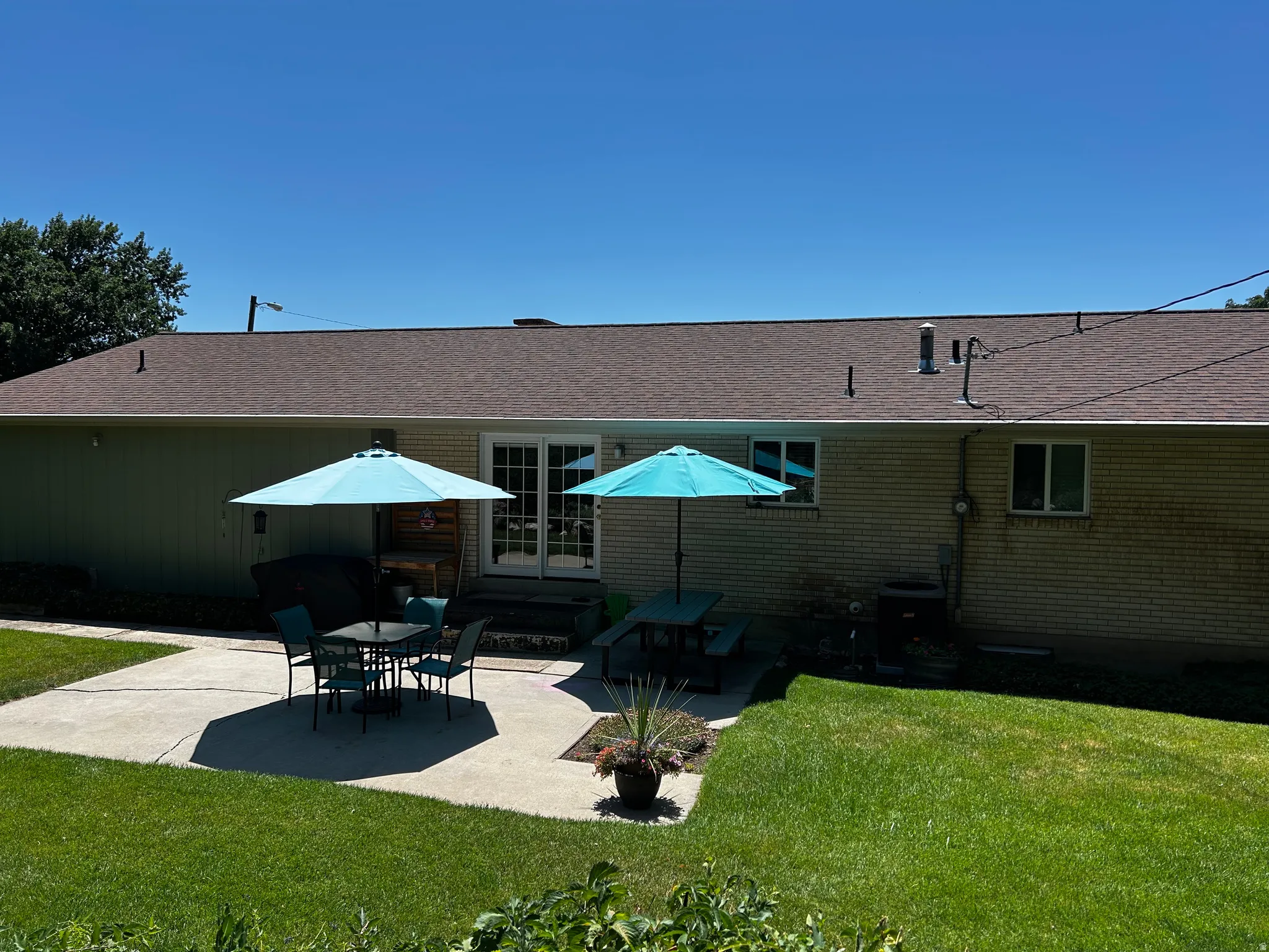 Rear view of house featuring a patio area, roof with shingles, and a lawn