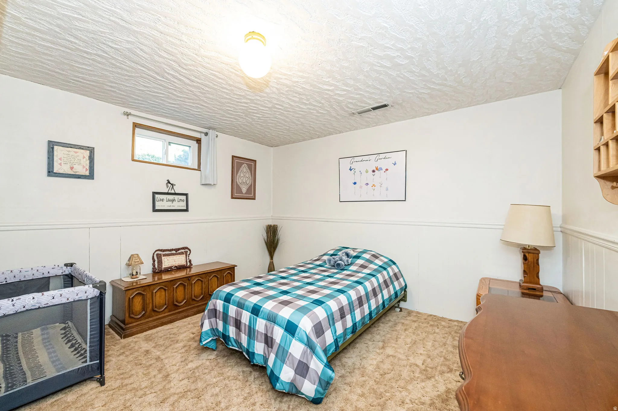 Carpeted bedroom with a wainscoted wall, a textured ceiling, and a decorative wall