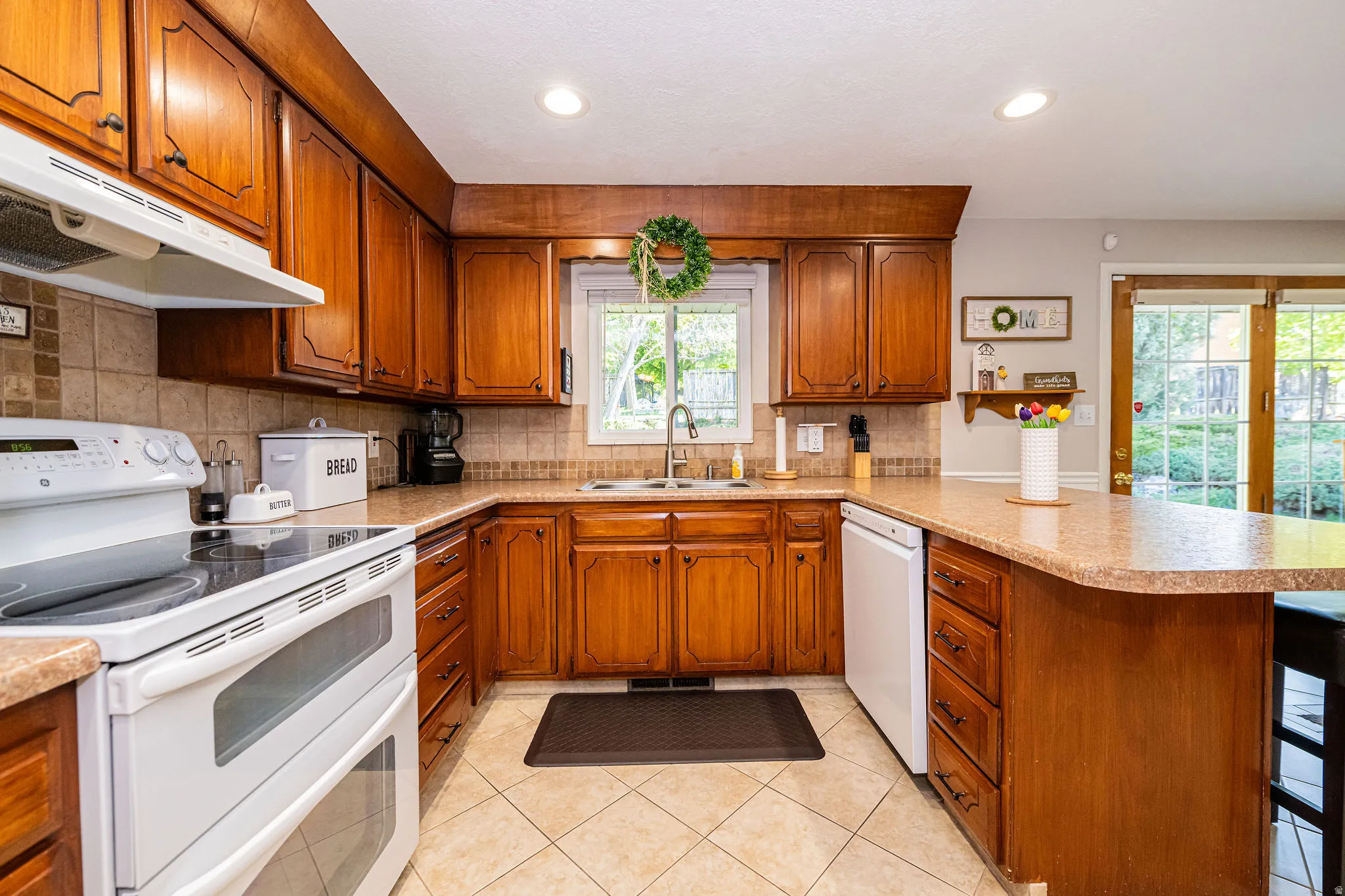 Kitchen featuring brown cabinetry, white appliances, a peninsula, light countertops, and recessed lighting