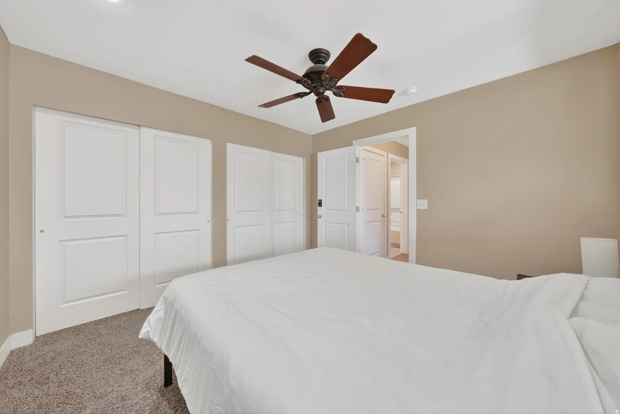 Bedroom featuring light colored carpet, a ceiling fan, and two closets
