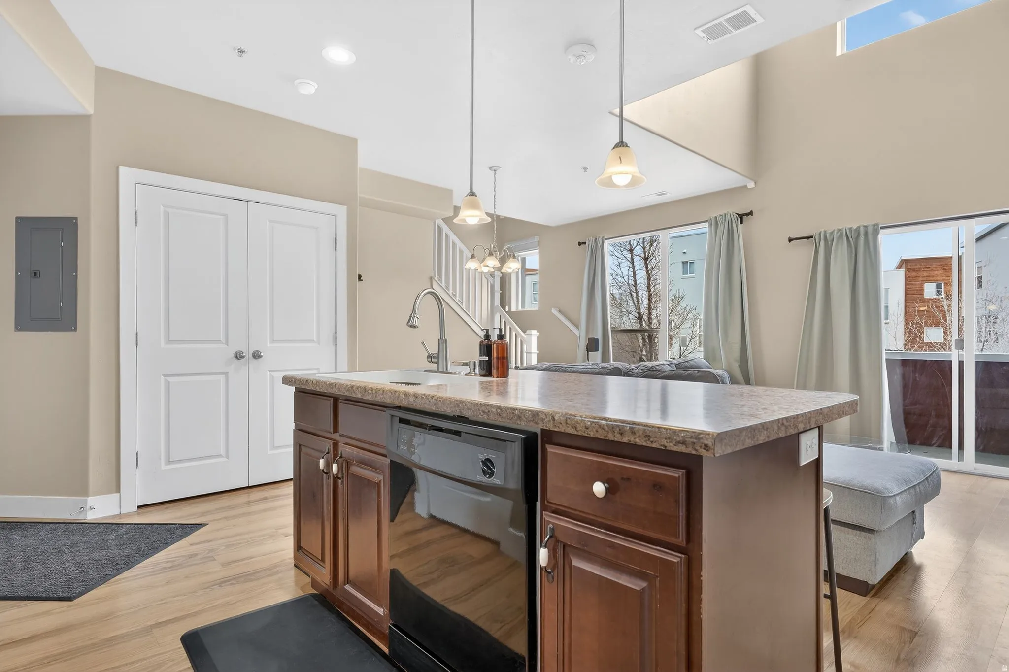 Kitchen with a center island with sink, hanging light fixtures, dishwasher, light countertops, and electric panel