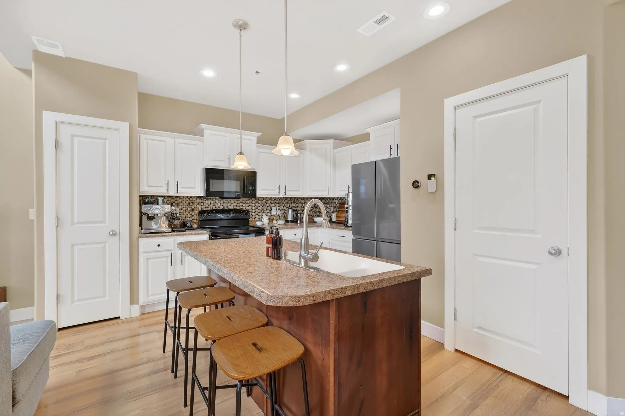 Kitchen with hanging light fixtures, white cabinetry, light wood finished floors, a center island with sink, and black appliances