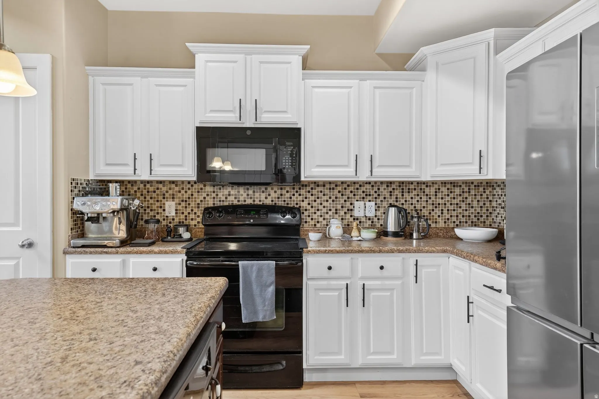 Kitchen with white cabinets, black appliances, backsplash, light stone counters, and hanging light fixtures