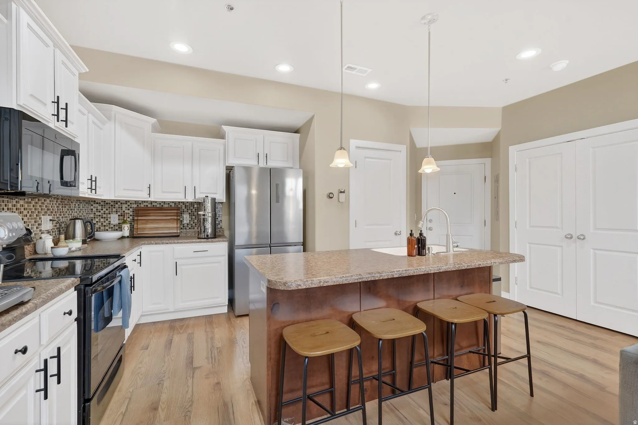 Kitchen with black appliances, a kitchen island with sink, light wood-type flooring, white cabinetry, and a kitchen breakfast bar