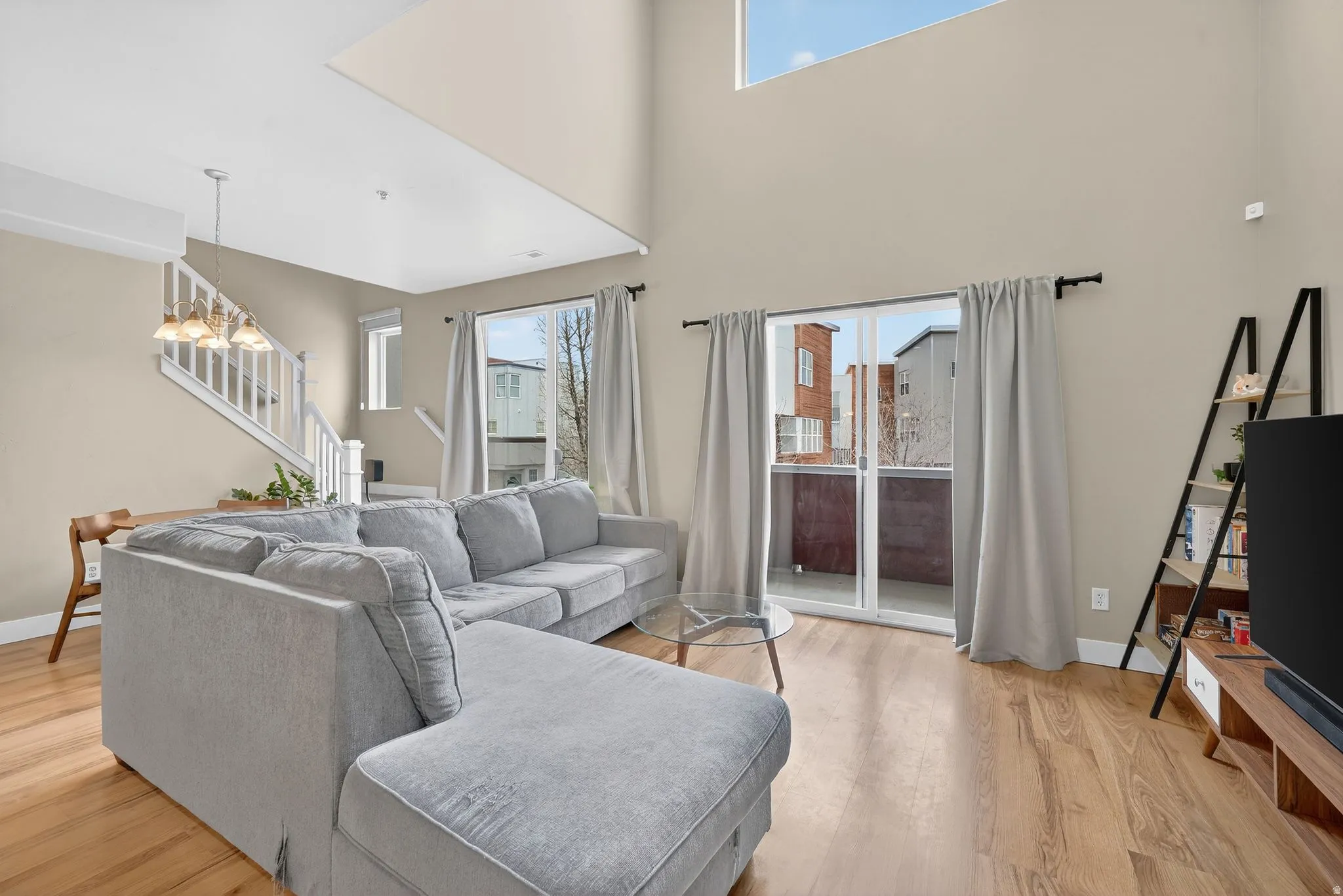 Living area with plenty of natural light, light wood finished floors, stairway, and a towering ceiling