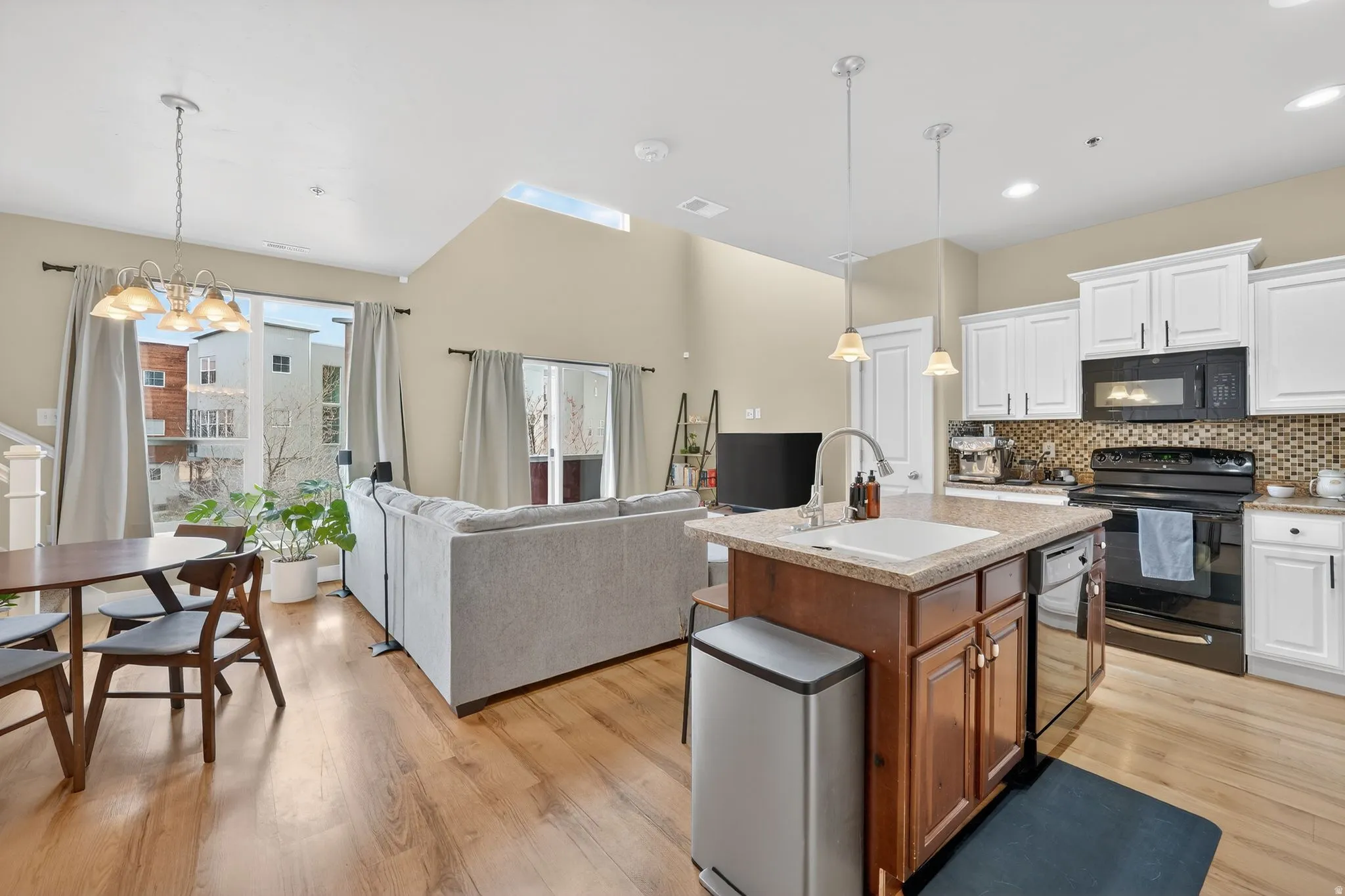 Kitchen with hanging light fixtures, black appliances, open floor plan, white cabinetry, and tasteful backsplash