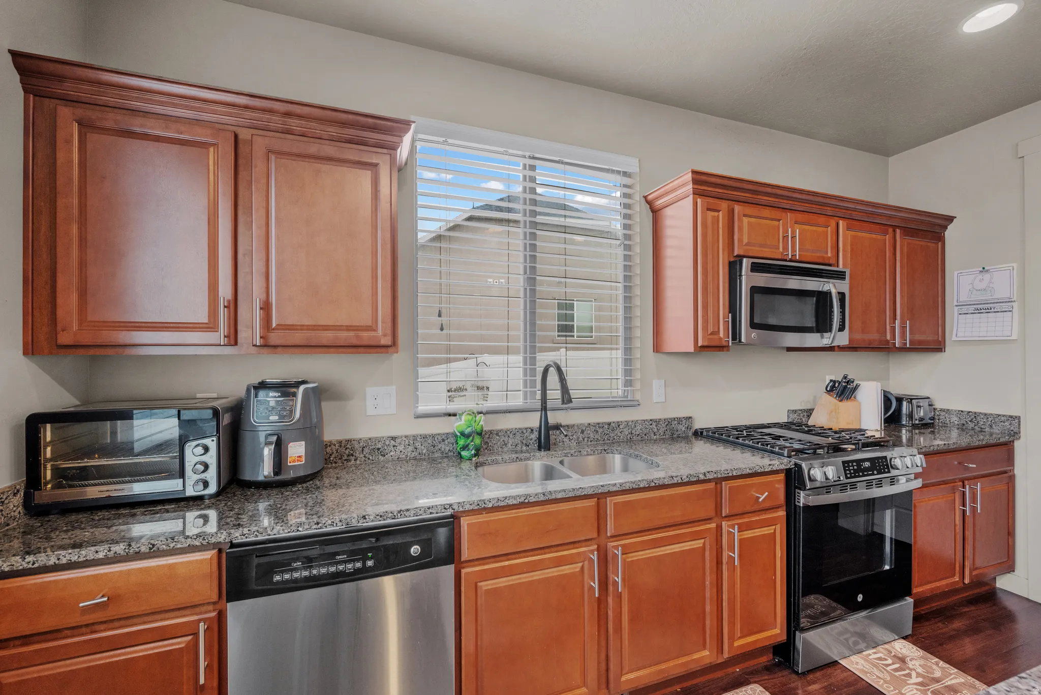 Kitchen featuring stainless steel appliances, dark stone countertops, wood finish cabinetry, and dark wood-style floors