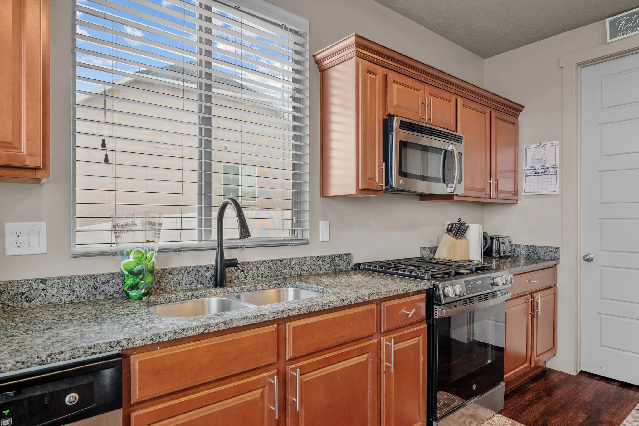 Kitchen featuring stainless steel appliances, light stone countertops, wood finish cabinets, and dark wood-style floors