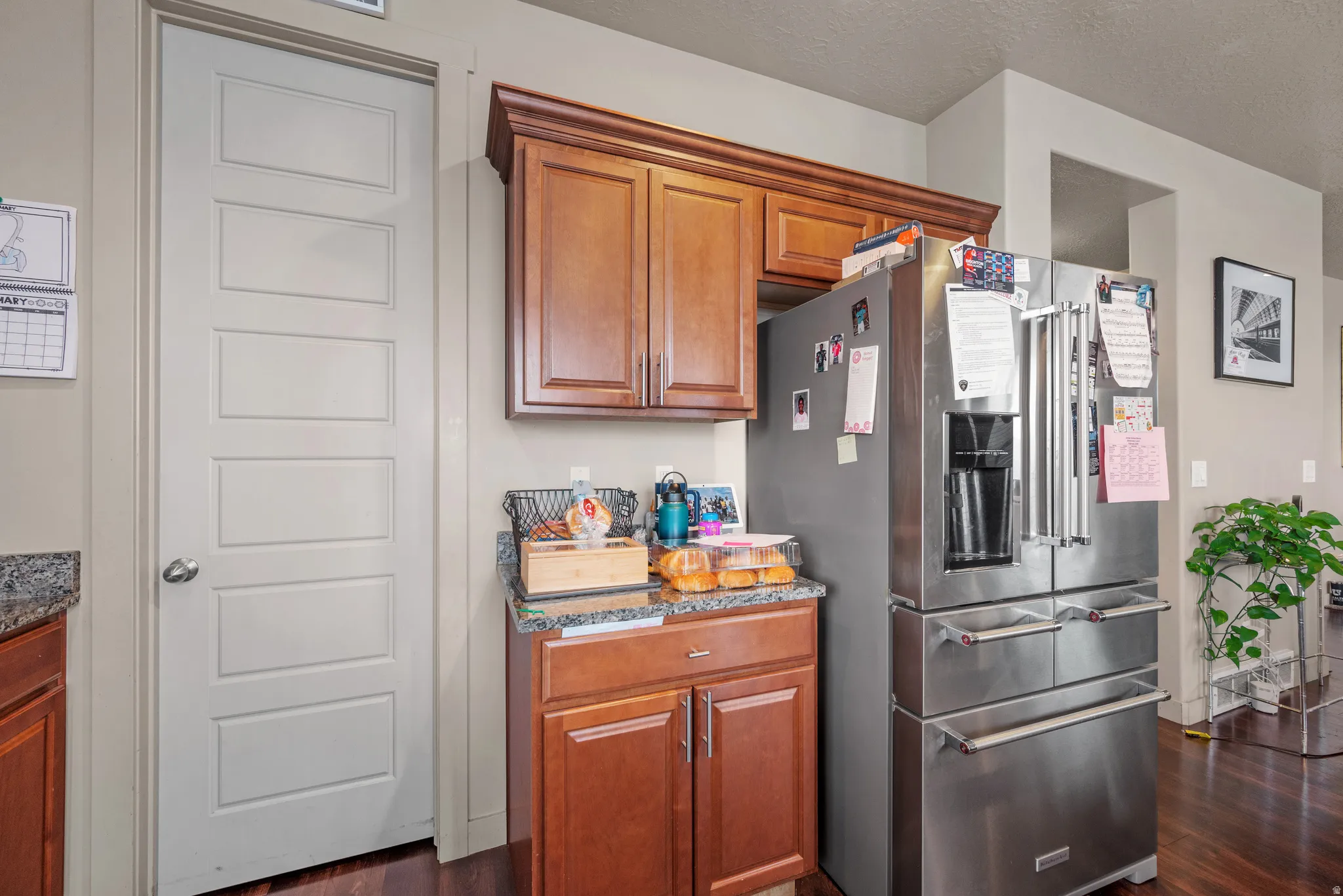 Kitchen featuring high end refrigerator, dark stone countertops, wood finish cabinets, dark wood-style flooring, and a textured ceiling