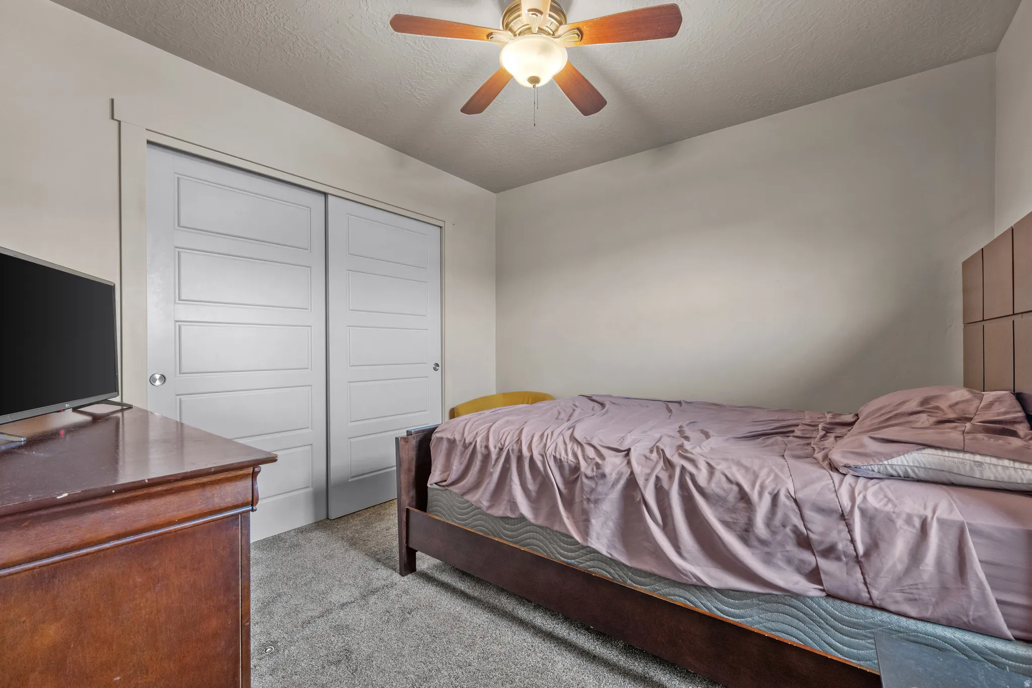 Bedroom featuring light carpet, a textured ceiling, a ceiling fan, and a closet