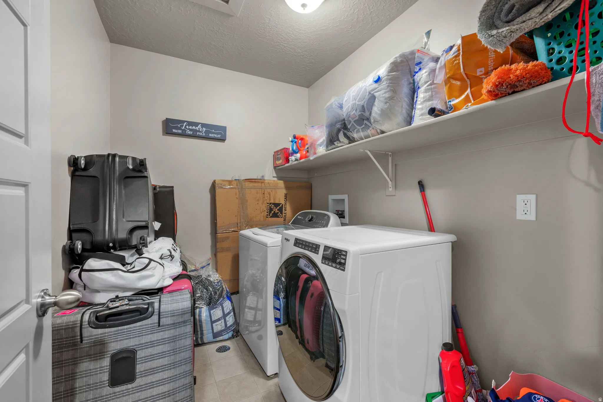 Laundry area featuring a textured ceiling, washer and dryer, and light tile patterned floors