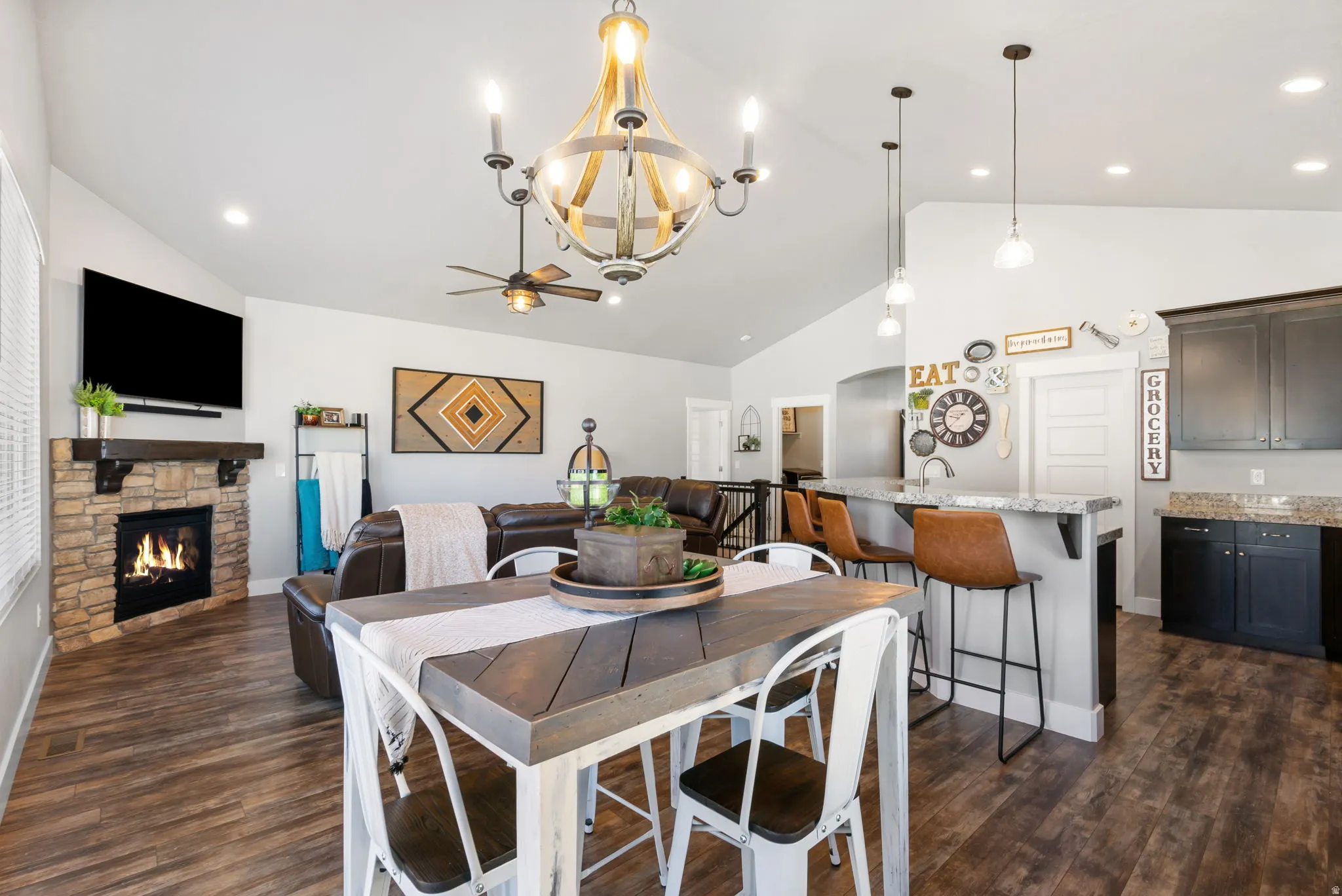 Dining room with dark wood-style floors, recessed lighting, a stone fireplace, high vaulted ceiling, and a chandelier