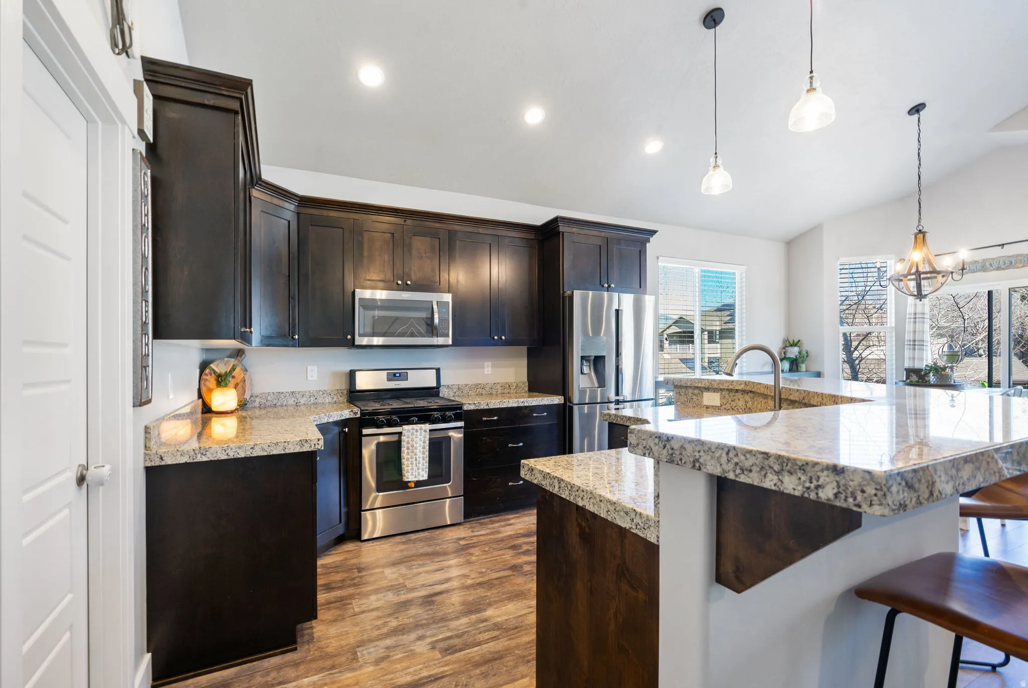 Kitchen with appliances with stainless steel finishes, lofted ceiling, pendant lighting, dark wood-type flooring, and dark brown cabinetry