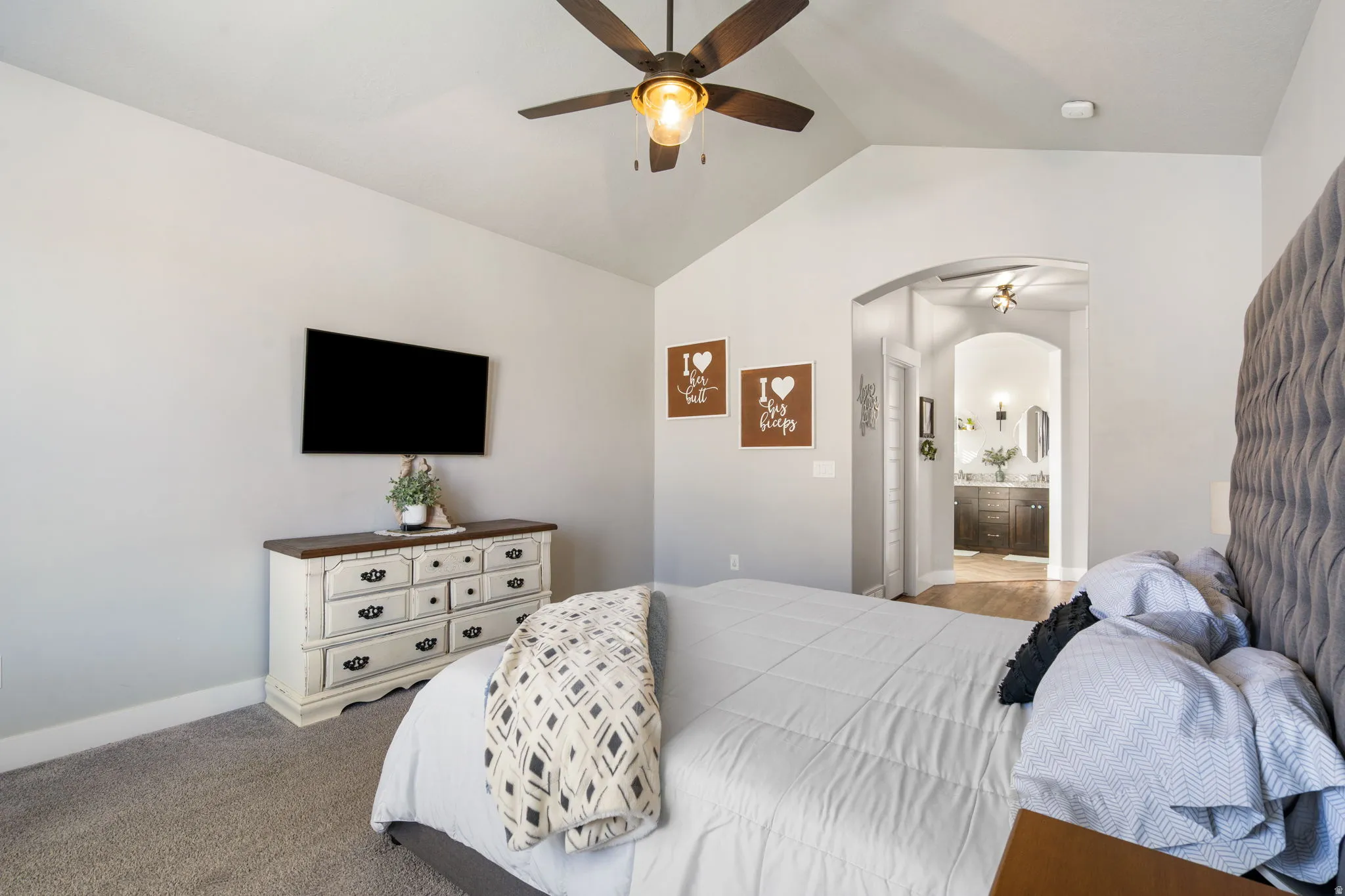 Carpeted bedroom featuring lofted ceiling, arched walkways, connected bathroom, and a ceiling fan