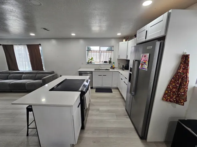 Kitchen featuring stainless steel appliances, open floor plan, a kitchen breakfast bar, white cabinetry, and recessed lighting