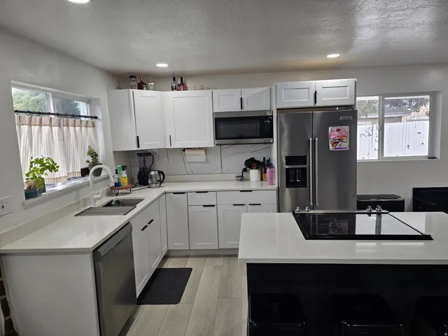 Kitchen with appliances with stainless steel finishes, light stone countertops, white cabinetry, light wood-style flooring, and recessed lighting