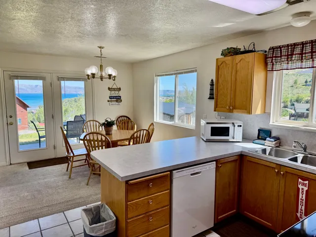 Kitchen and dining area featuring a double basin sink, light wood cabinetry, white dishwasher, and light-toned countertops