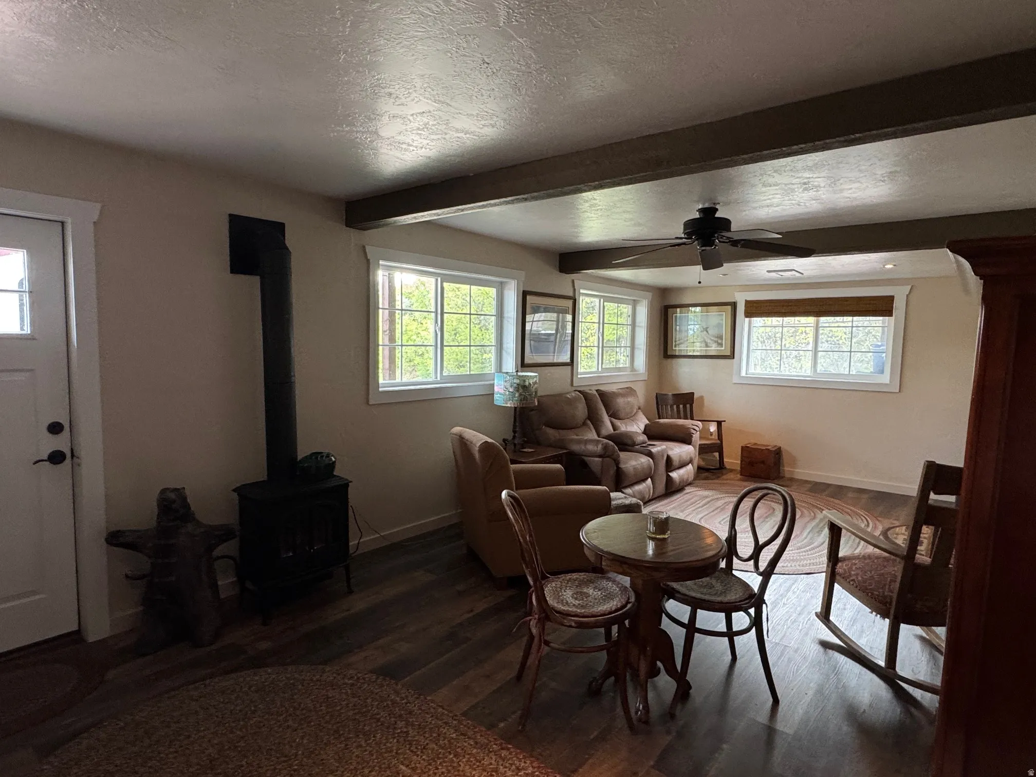 Family Room dark wood finished floors, a wood stove, beam ceiling, and a ceiling fan