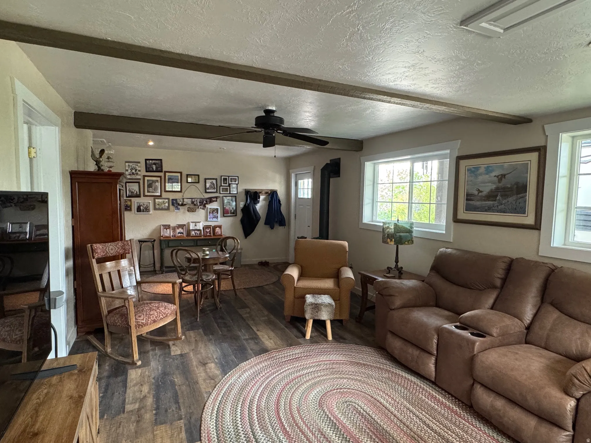 Family Room dark wood finished floors, a wood stove, beam ceiling, and a ceiling fan