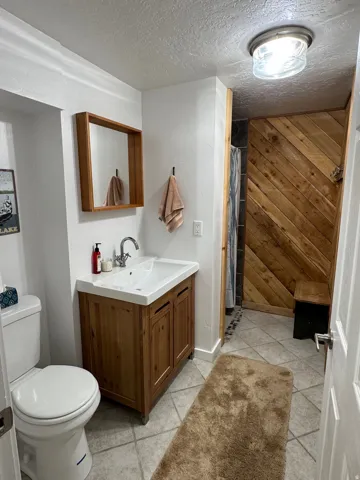 Bathroom with wood walls, tiled shower, vanity, a textured ceiling, and light tile patterned flooring