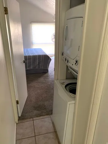 Laundry area featuring light colored carpet, stacked washer / drying machine, and light tile patterned floors